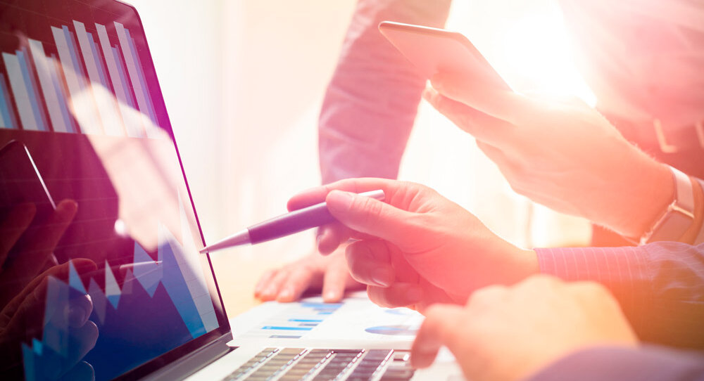 Mehrere Hände interagieren mit einem Laptop, während Diagramme und Grafiken auf dem Bildschirm angezeigt werden.
