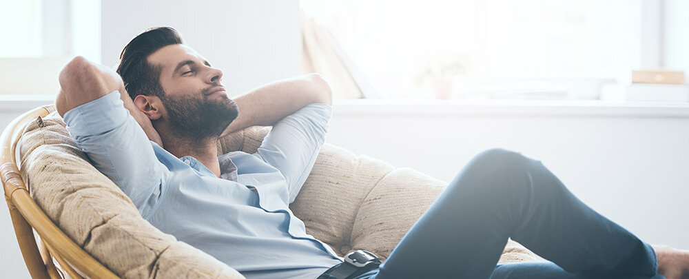 Ein Mann sitzt entspannt in einem großen, runden Sessel und genießt einen Moment der Ruhe in einem hellen Raum.