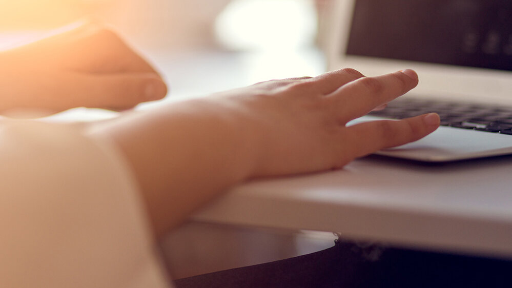 Eine Hand liegt sanft auf der Tastatur eines Laptops, während warmes Licht den Raum erhellt und eine entspannte Atmosphäre schafft.