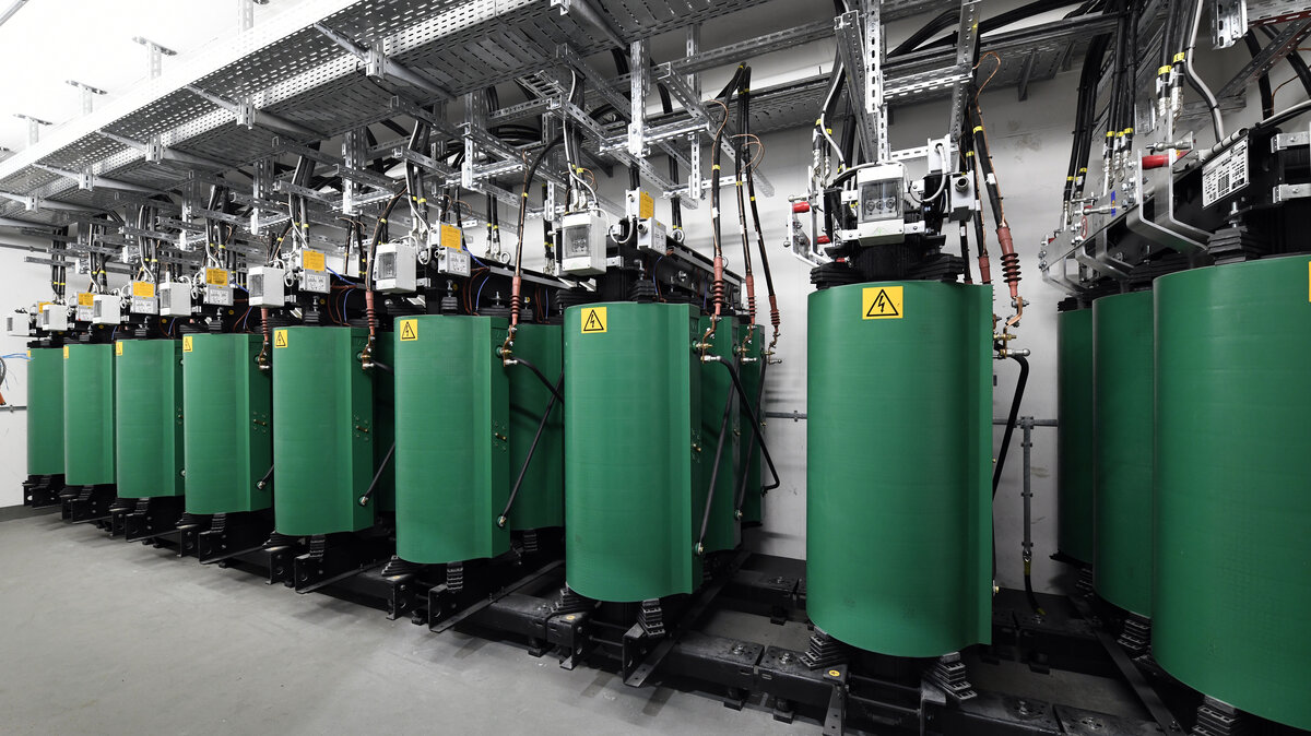 Eine Reihe von grünen Zylindern steht in einem modernen Raum, ausgestattet mit technischen Geräten und Warnschildern.