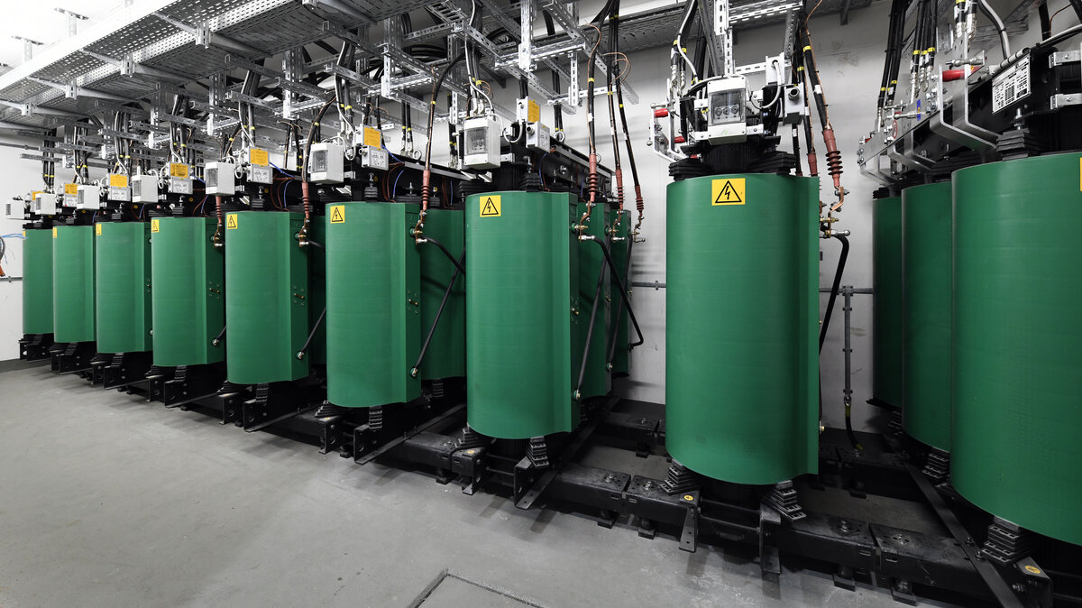 Eine Reihe von grünen Zylindern steht in einem modernen Raum, ausgestattet mit technischen Geräten und Warnschildern.