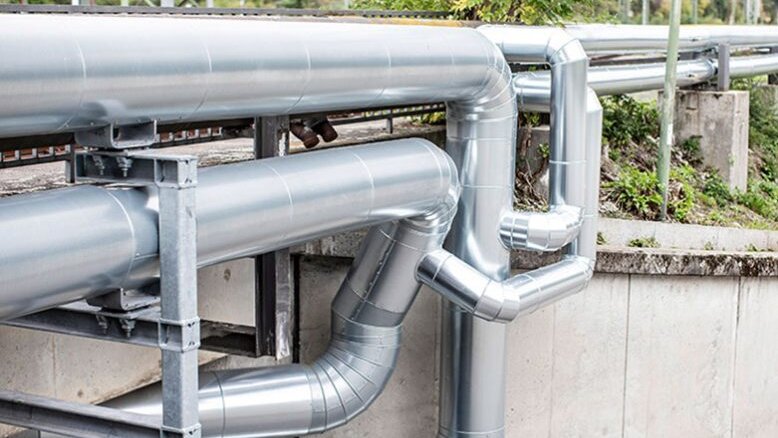 Eine komplexe Anordnung von glänzenden Metallrohren, die an einer Betonwand entlang verlaufen und in verschiedene Richtungen führen.