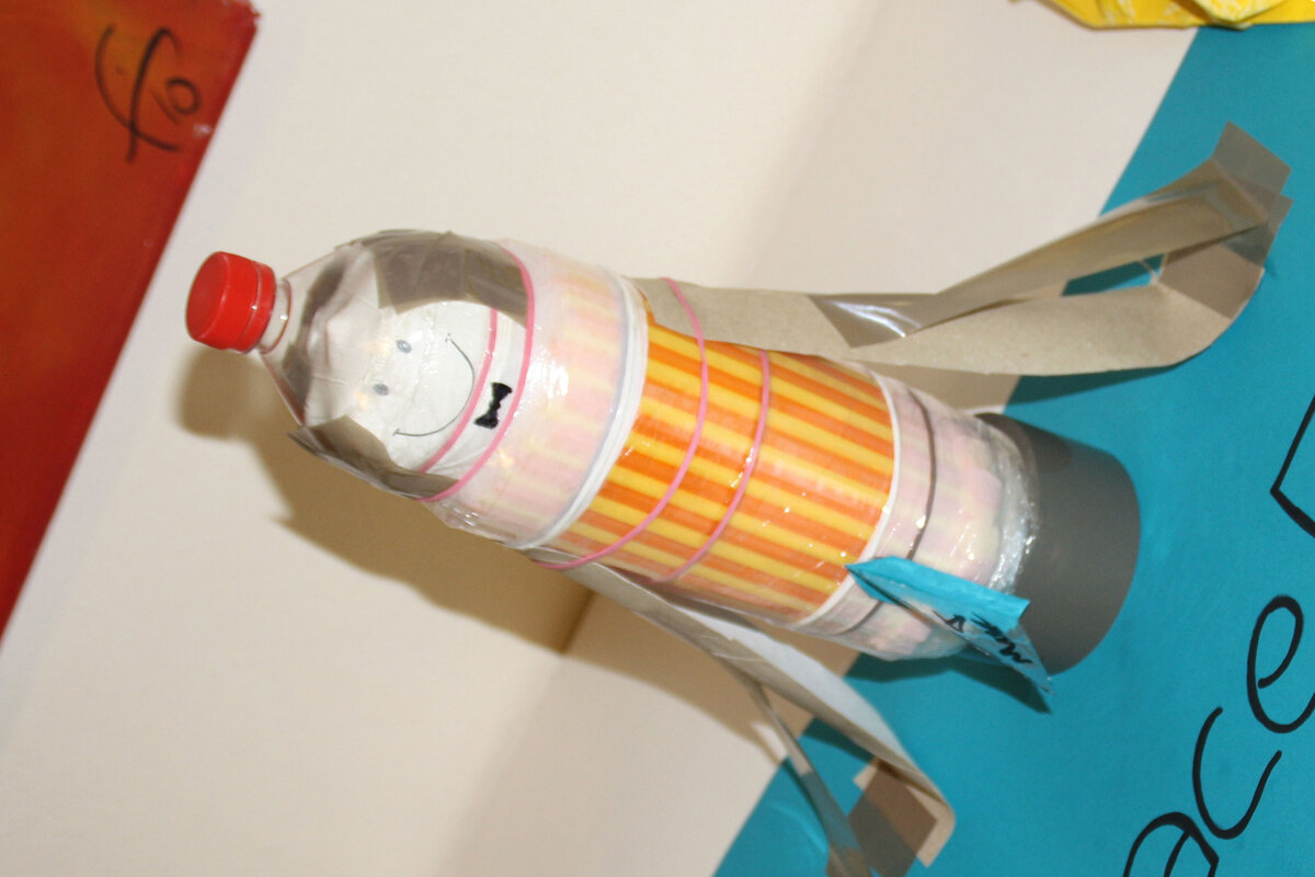 Ein originelles Kunstwerk: Eine Rakete aus einer Flasche, dekoriert mit bunten Bechern und einem freundlichen Gesichtsausdruck.