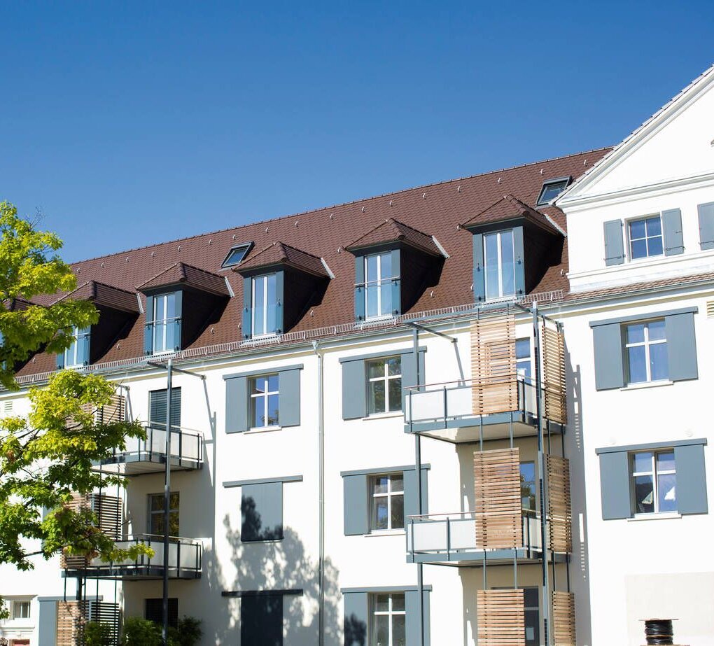 Die Architektur eines stilvollen Wohnhauses mit mehreren Etagen, großen Fenstern und einem schönen Baum im Vordergrund.