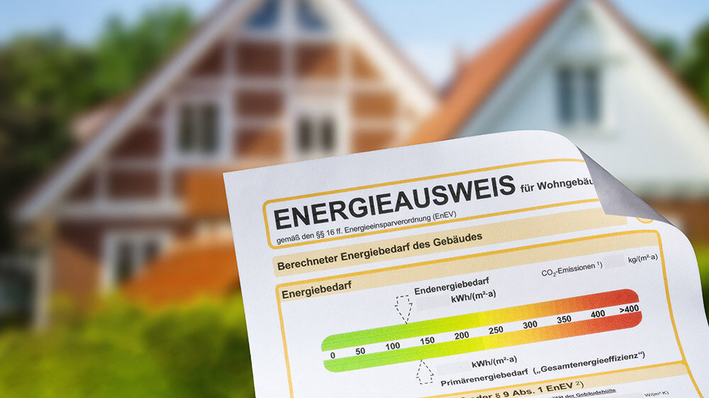 Im Vordergrund ist ein Energieausweis zu sehen, während ein klassisches Wohnhaus im Hintergrund steht.