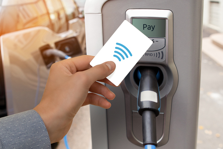 Eine Hand hält eine kontaktlose Karte, während sie an einer Ladestation für Elektrofahrzeuge bezahlt.