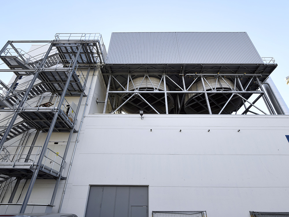 Ein Blick auf eine industrielle Struktur mit Kühltürmen, die durch ein metallisches Gerüst und Treppen zugänglich sind.