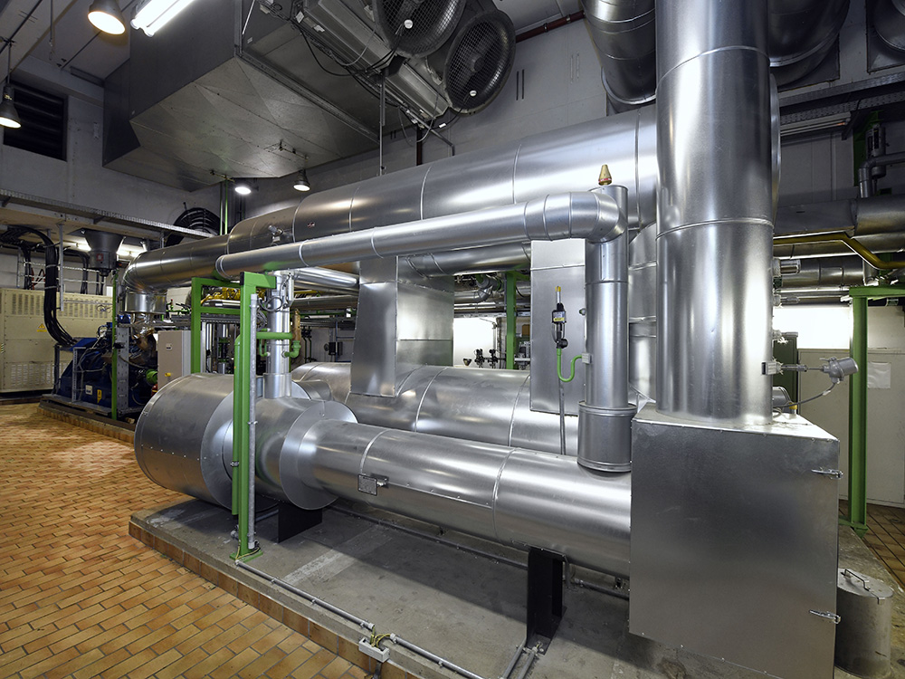 Komplexe Rohrleitungen aus Edelstahl verlaufen durch einen großen Raum, der für technische Prozesse genutzt wird.