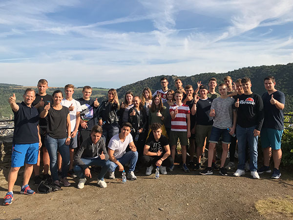 Eine Gruppe von Jugendlichen posiert fröhlich im Freien, alle zeigen Daumen hoch und lächeln in die Kamera.